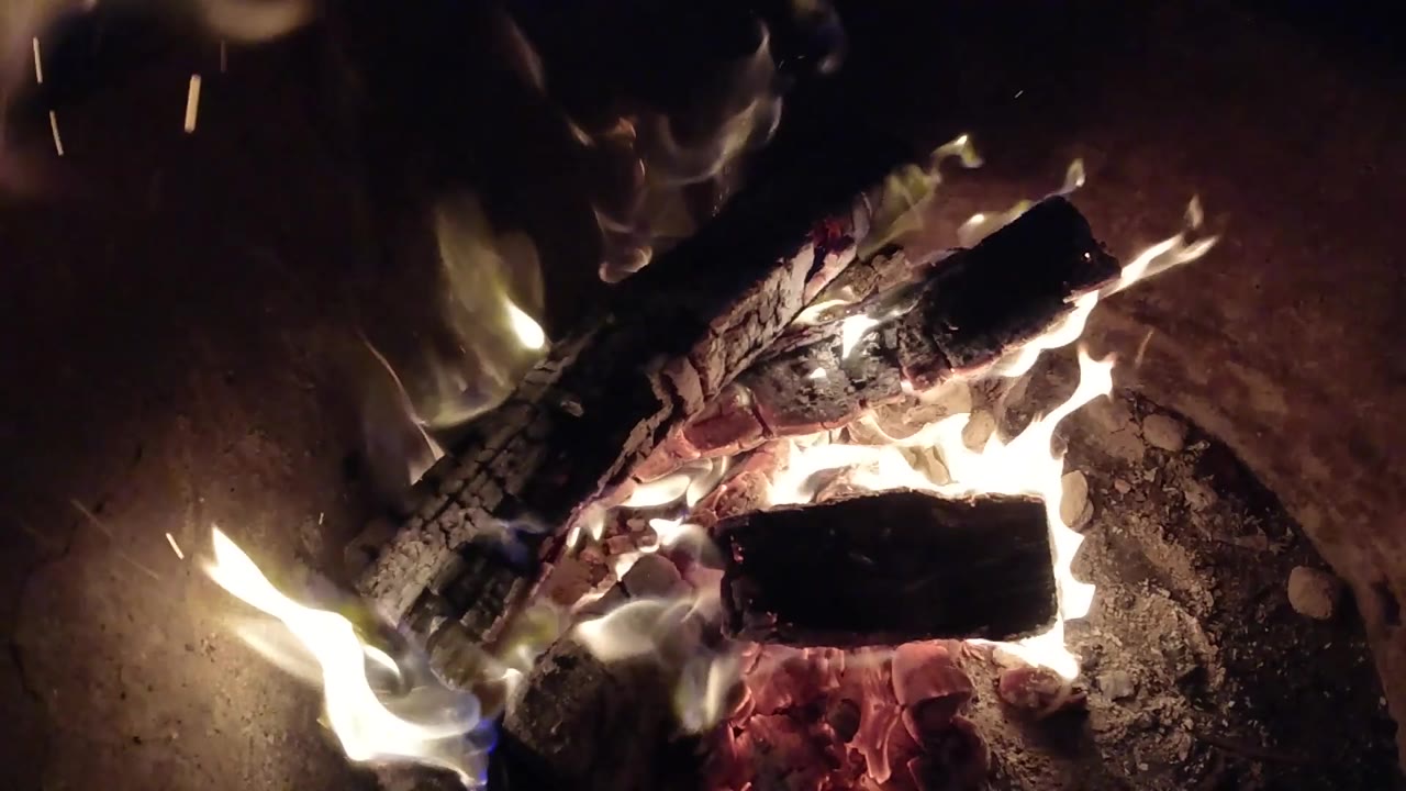 Active flames and sparks around charred logs.