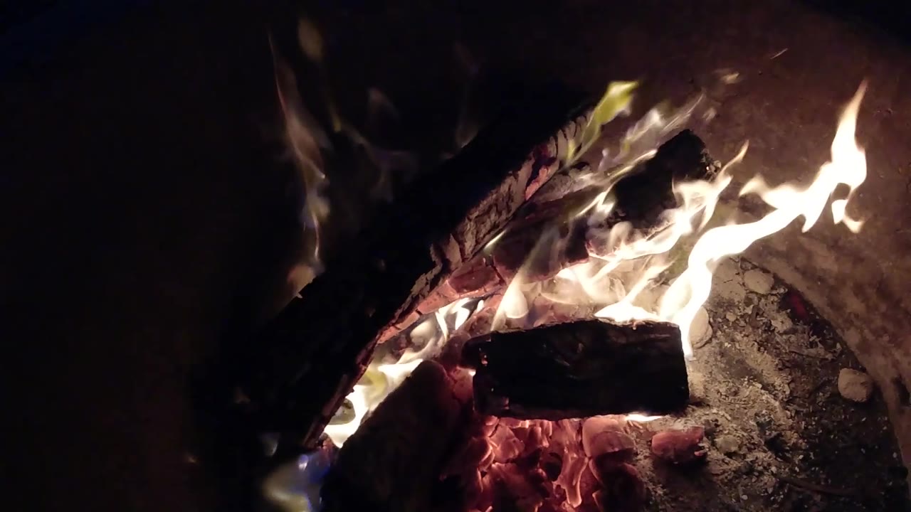 Tight Pismo Beach, California fire frame showing a long white-yellow flame crossing over blackened wood with ash to the right and no visible people.