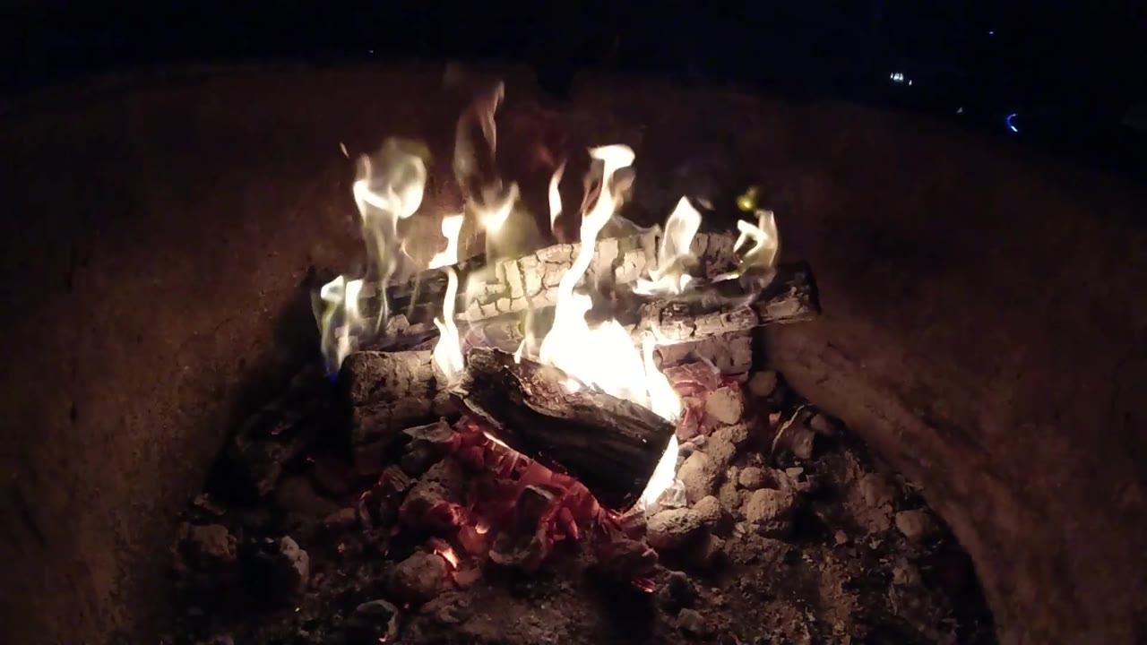At 0:03, flames lean across the blackened wood while glowing embers cluster beneath in the Pismo Beach fire scene, with no visible people.