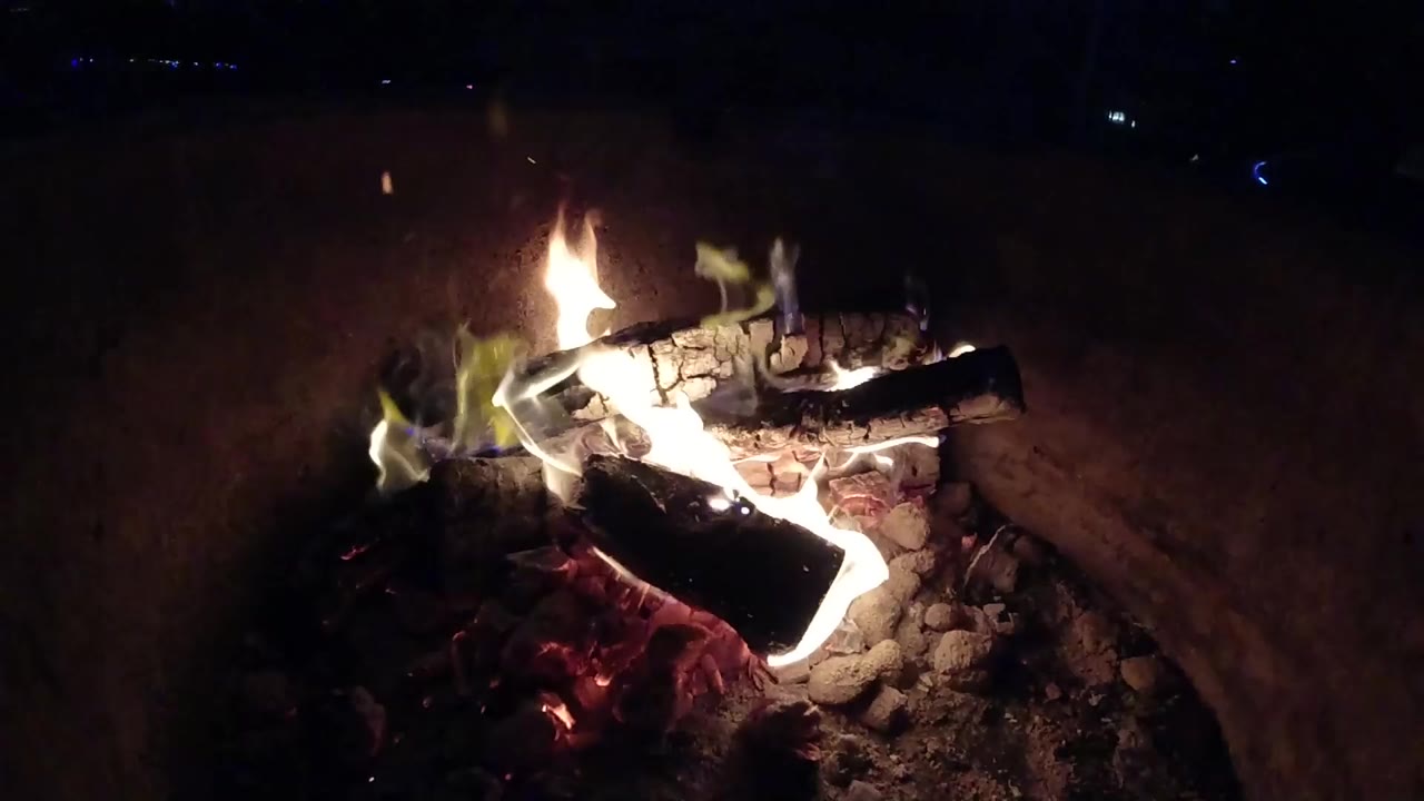 Burning logs over embers in a dark fire pit.