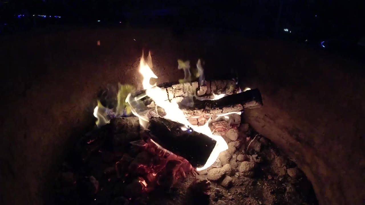 At one second, the Pismo Beach clip shows flames wrapping the front log while a charred log rests across the top and no visible people appear.
