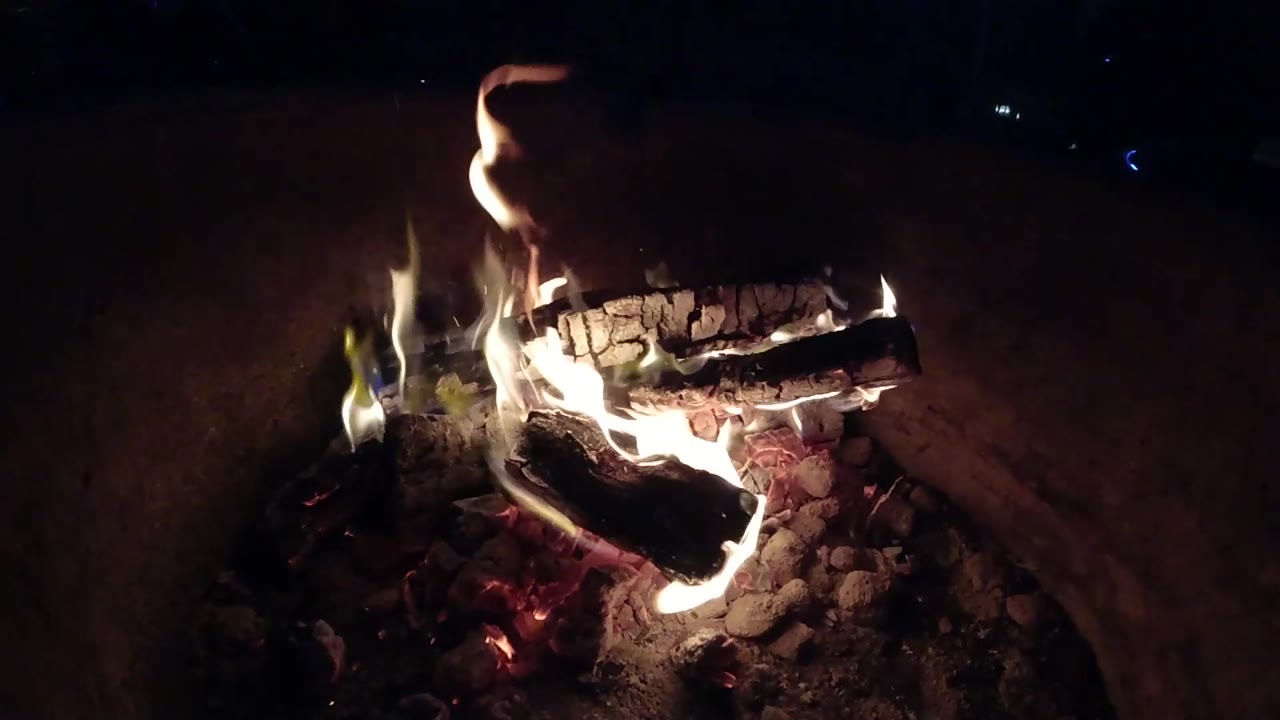 At two seconds, a taller flame lifts above the upper log in the Pismo Beach fire pit, with stones and embers below and no visible people.