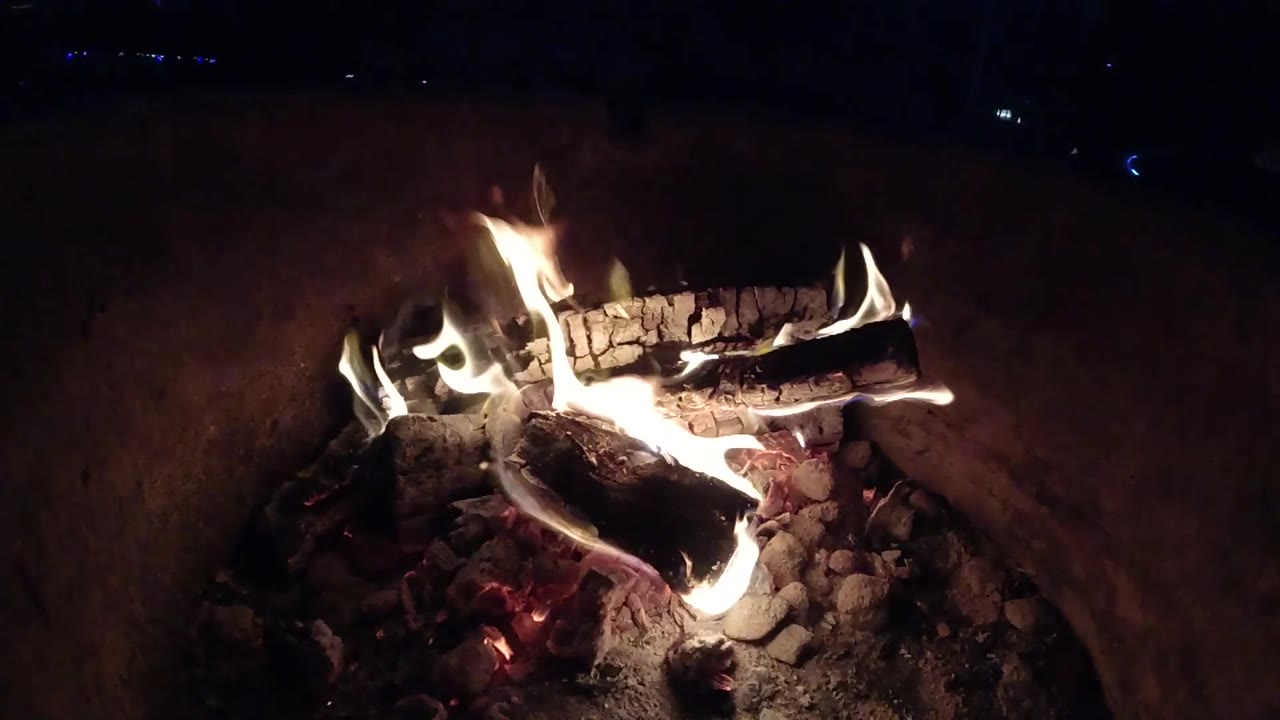 At three seconds, bright flames run along two crossed logs in the Pismo Beach nighttime fire, with a dark rim around the pit and no visible people.