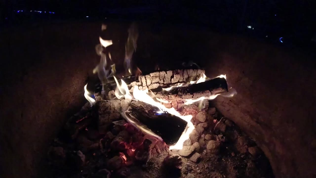 Flames rise around stacked wood over red coals.