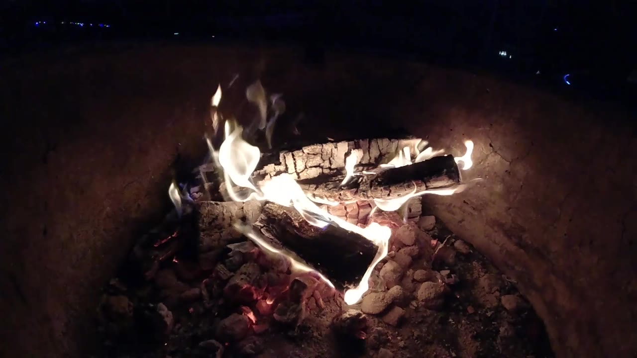 At 0:02, bright flames curl across the horizontal log and light the curved fire pit wall in Pismo Beach, California, with no visible people.