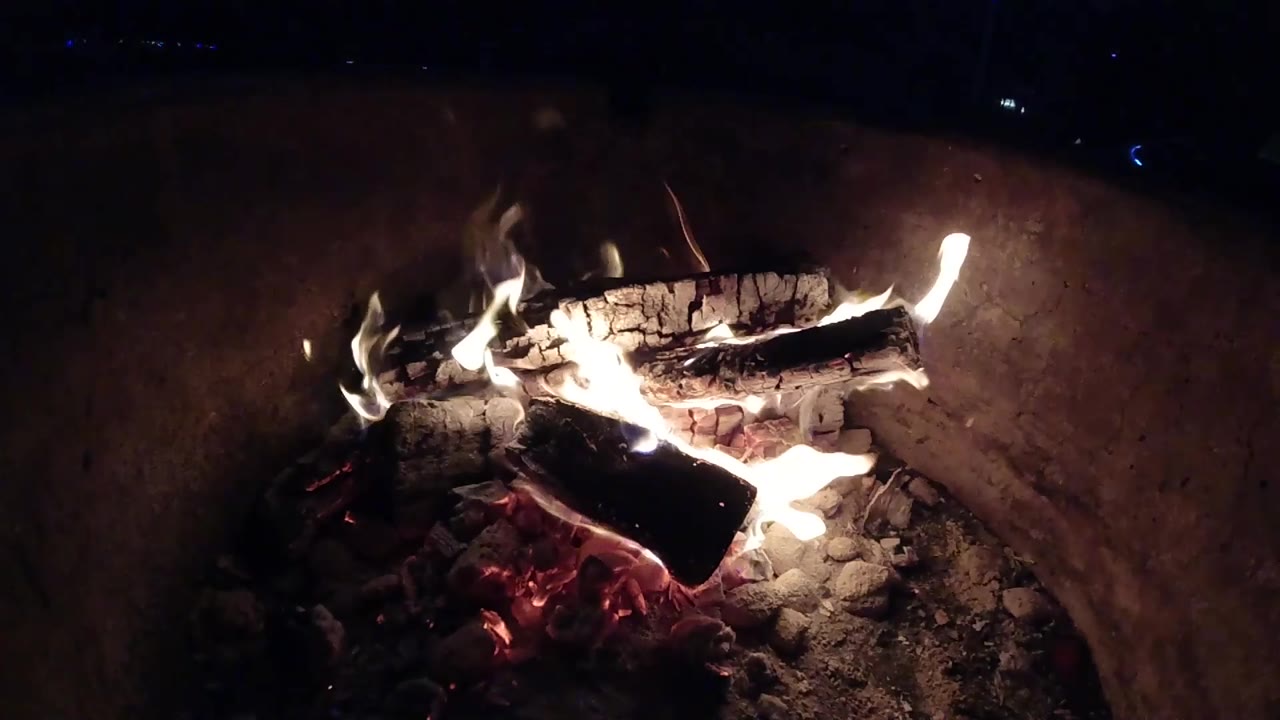 In Pismo Beach, California, a bright flame licks across the front of the campfire while the larger log rests over ash and embers, with no visible people.