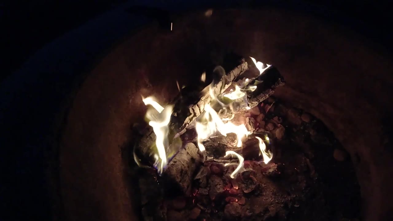 At 0:02, flames flare along the left side of the burning logs while the round fire pit edge stays mostly in shadow in Pismo Beach, California, with no visible people.