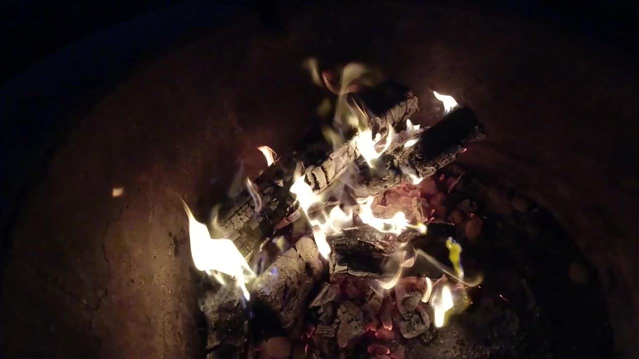 Burning logs and flames inside a dark fire pit.