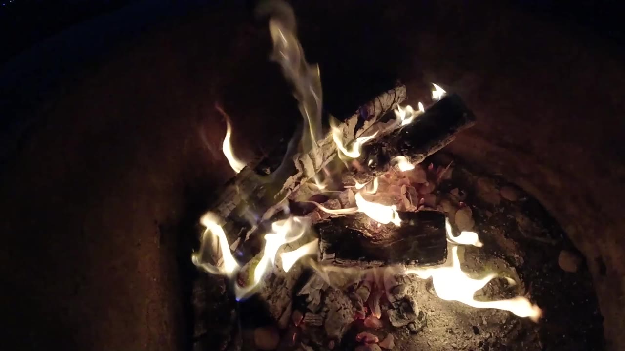 At 0:01, brighter flame tongues wrap around the central logs and ash in the Pismo Beach campfire, with no visible people.