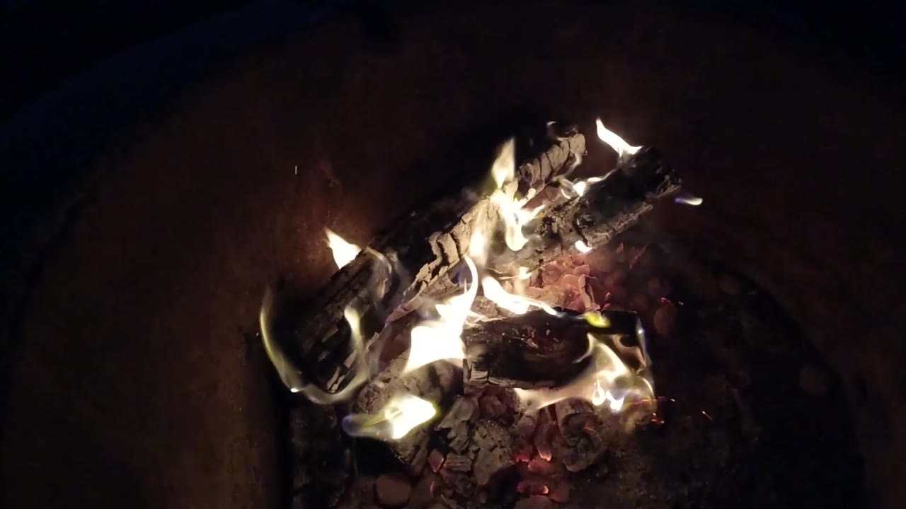 Flames rising around two dark logs over embers