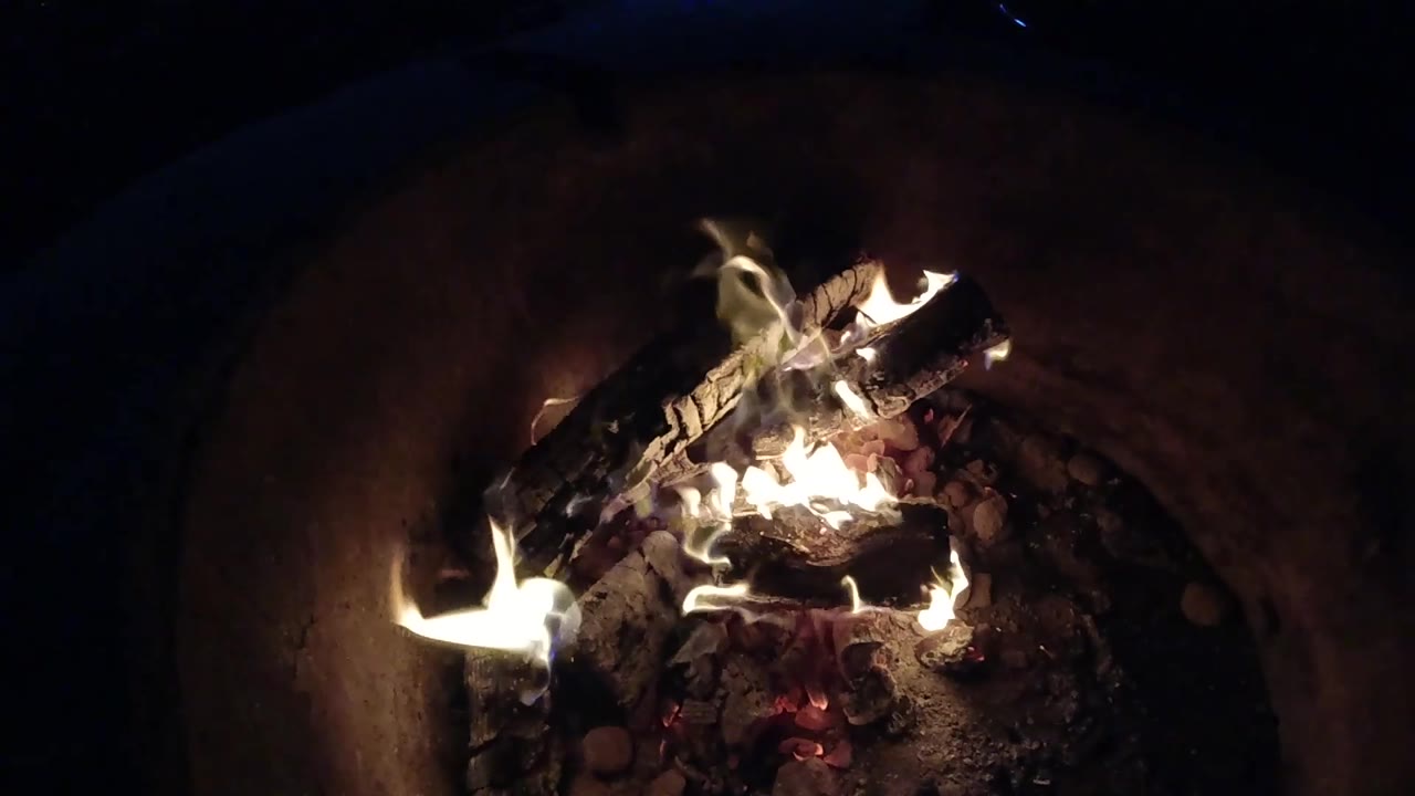 At 0:02, a brighter tongue of flame flares along the left side of the burning logs in the Pismo Beach fire pit, with no visible people in frame.