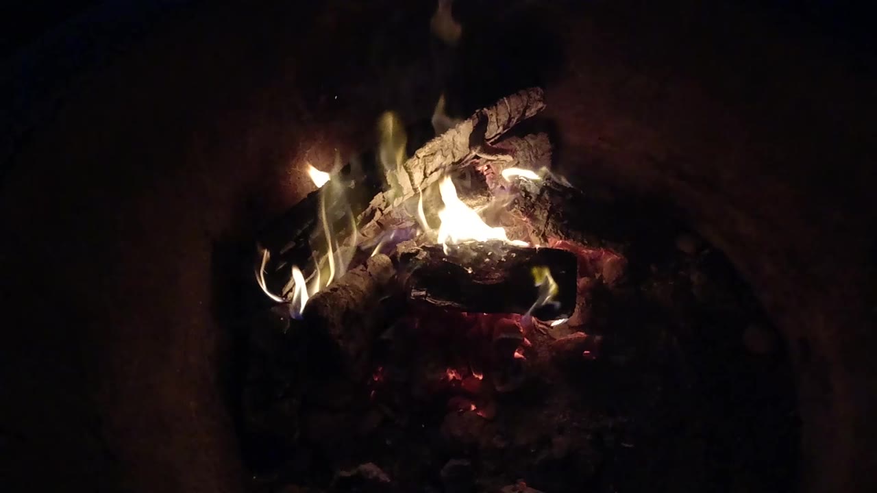 Flames curling over charred wood above red embers.