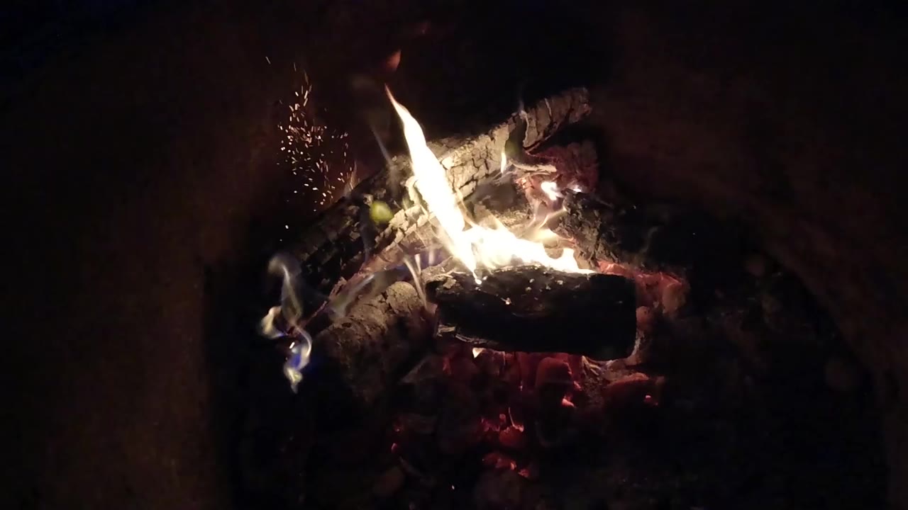 Burning logs glow with white flames and red embers in a dark Pismo Beach fire scene, with no visible people in this frame.