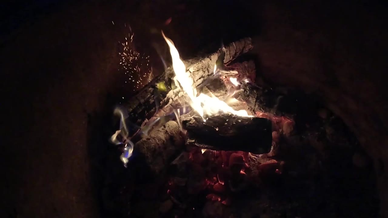Flames curl over charred wood above glowing embers.
