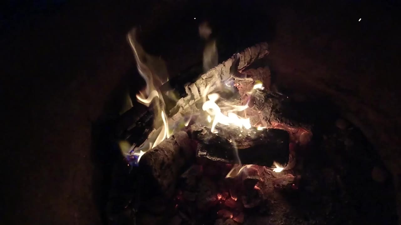Small fire burning on dark logs and embers