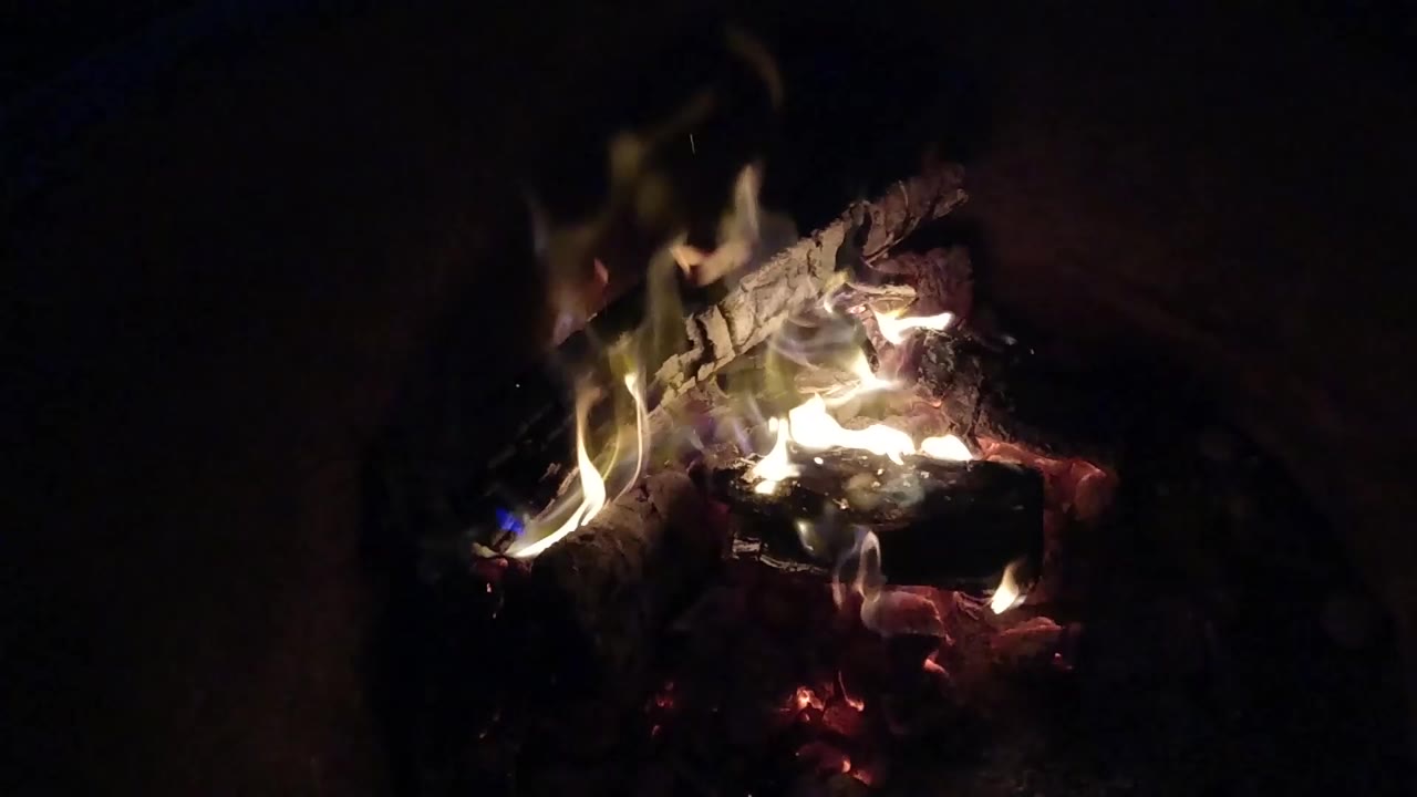 At 0:00 in the Pismo Beach, California clip, small pale flames rise from charred wood above red embers, with no visible people.