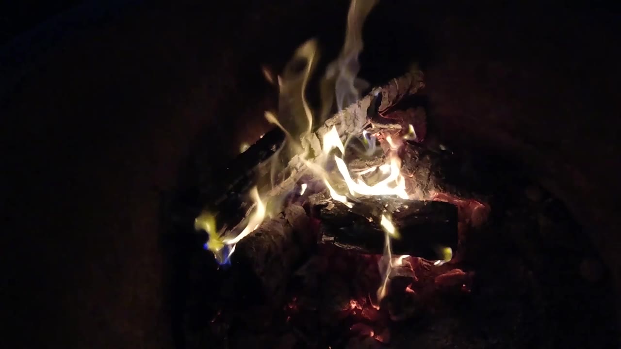 At 0:02, taller yellow and white flames lift from the left side of a charred log in Pismo Beach, California, with no visible people.