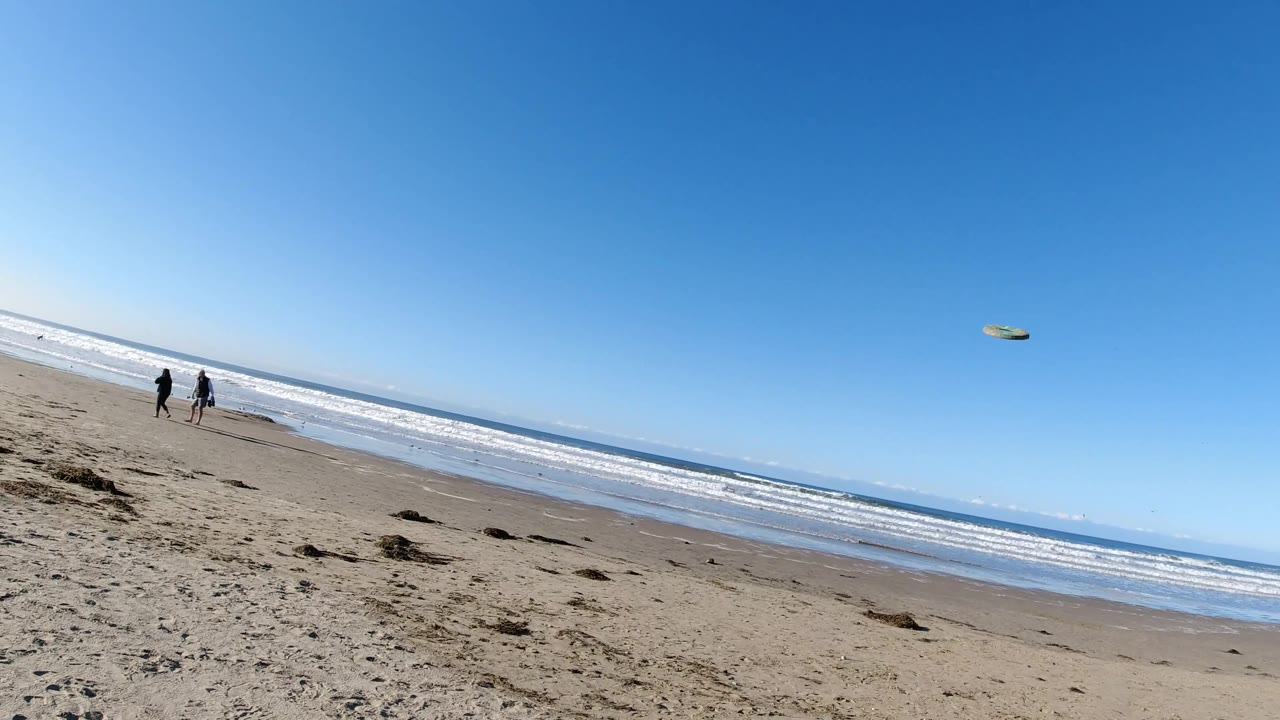 Pismo Beach, California beach frame with a yellow disc visible in the upper right sky, two distant people by the waterline, and a slanted horizon over breaking waves.