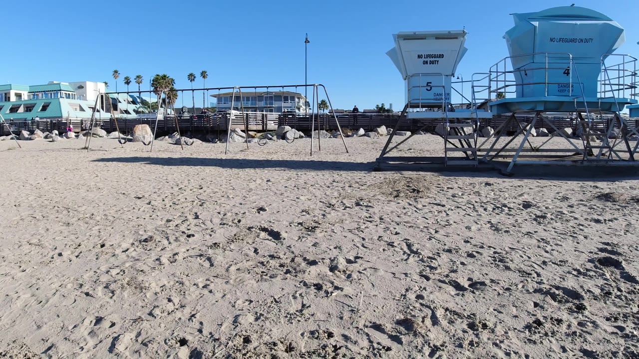 Two lifeguard towers and beach structures beside open sand.