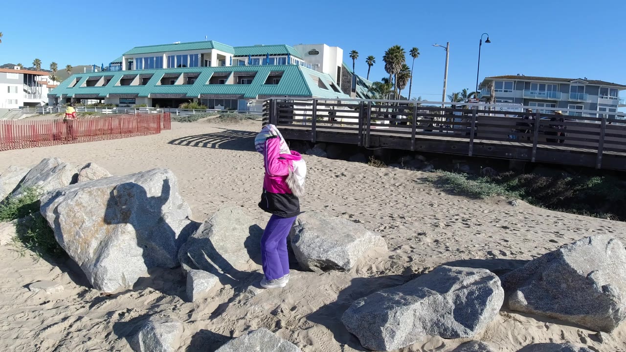 Child in bright clothing standing among rocks on sandy beach.