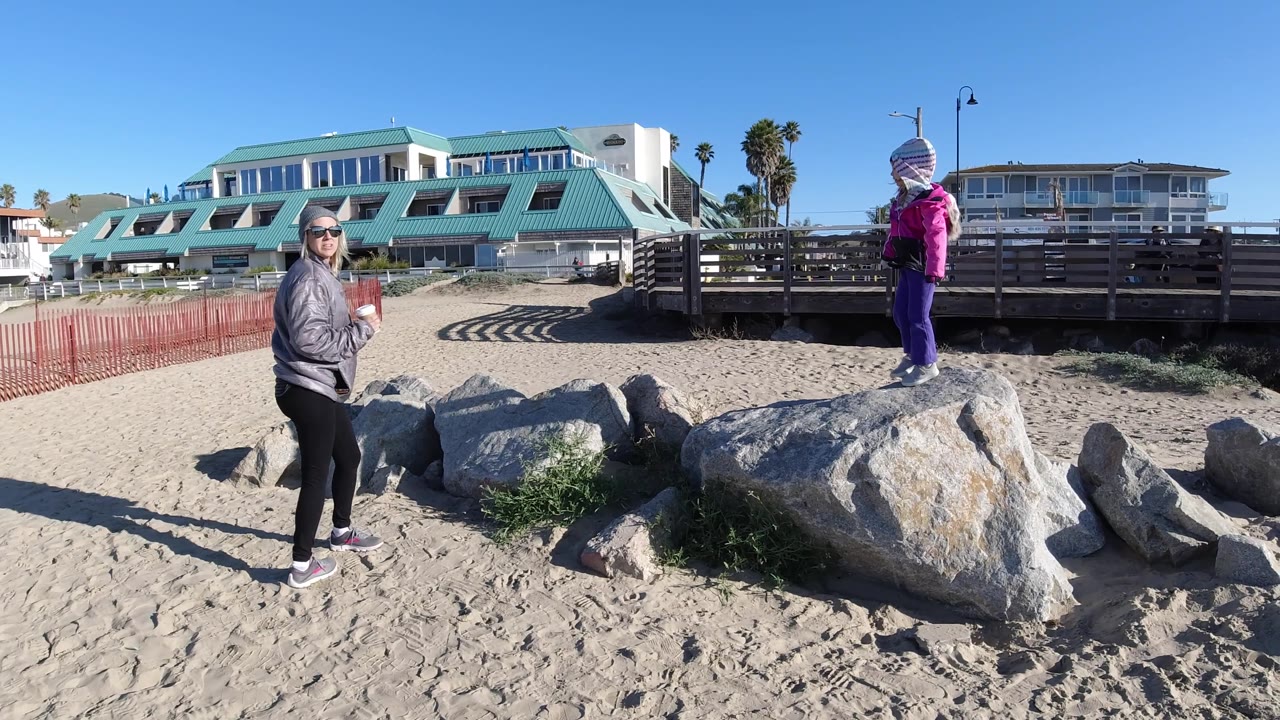 Woman holding cup stands beside rocks while child stands on boulder.