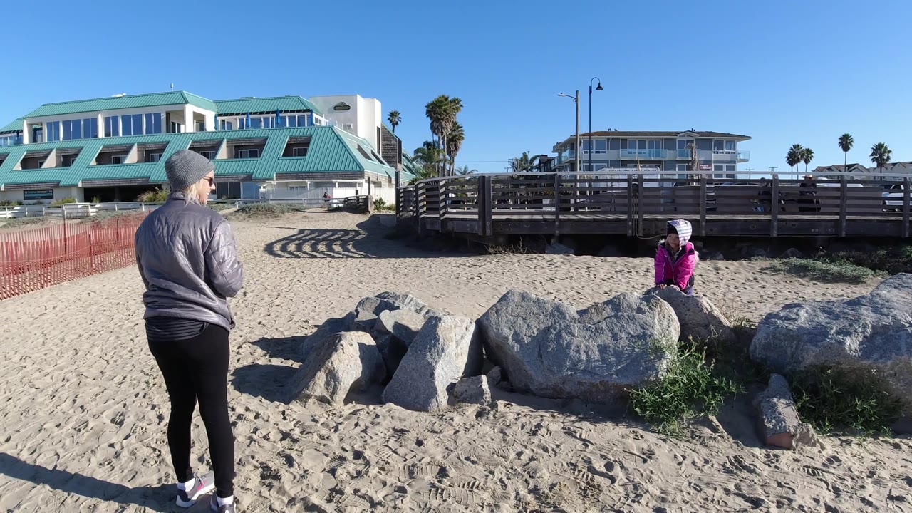 Person in gray jacket standing left of frame, person in pink by rocks.