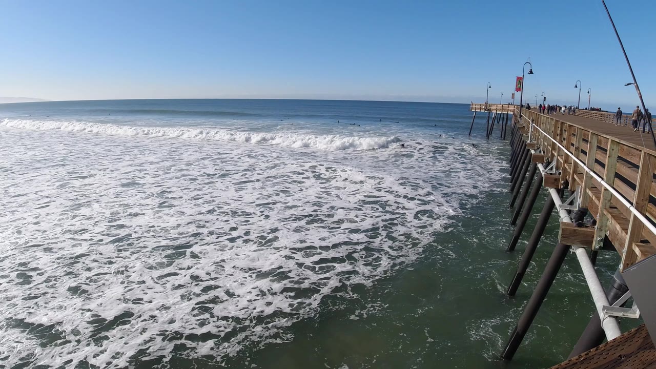 White surf foam rolls across ocean water next to pier pilings.