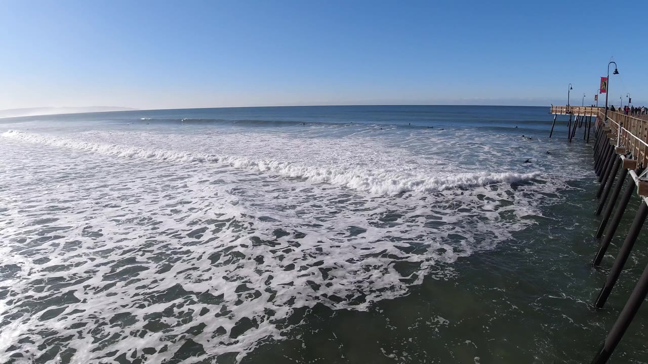White surf spreads across the ocean near a bridge railing.