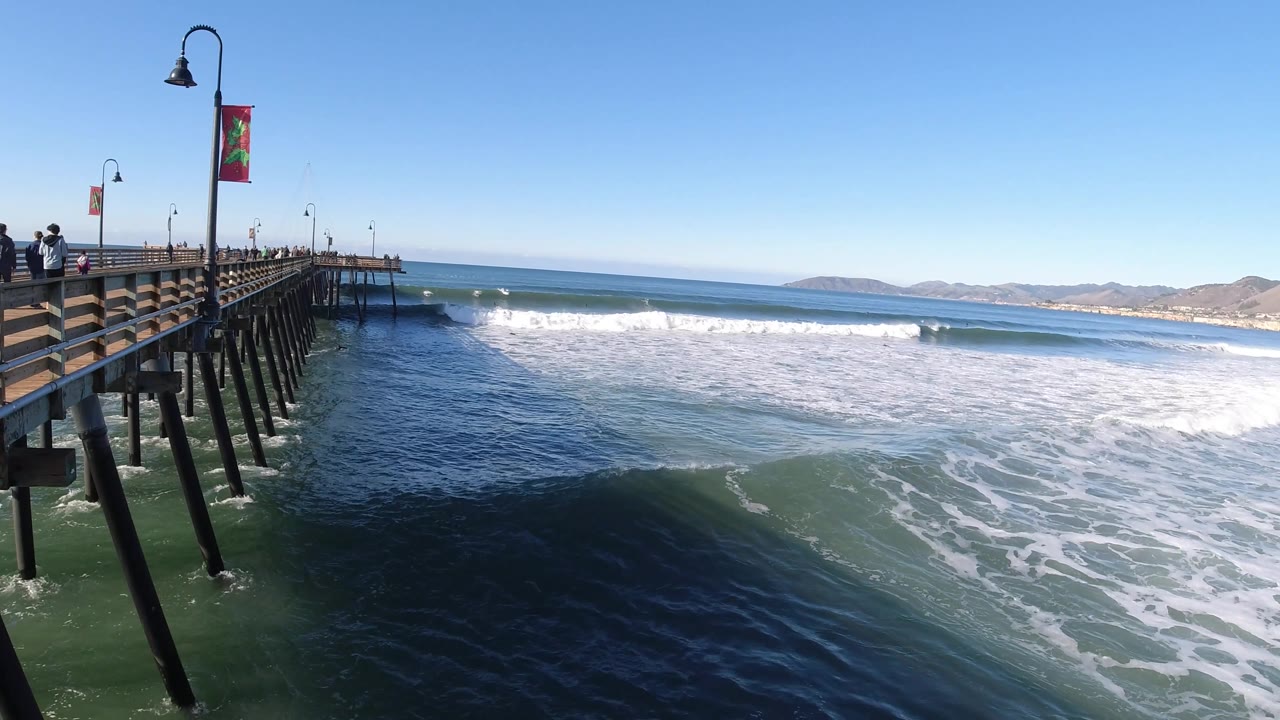 Foamy surf fills the water beside a long wooden pier.