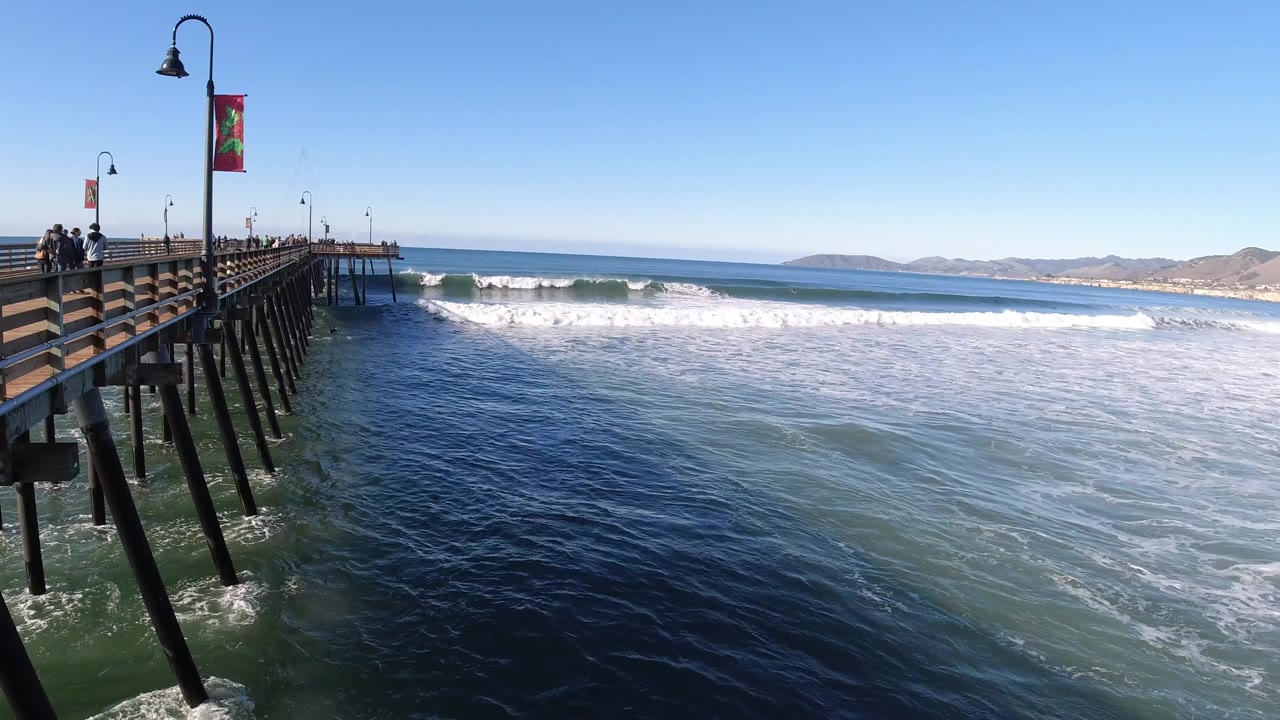 Pier beside breaking waves under a clear blue sky