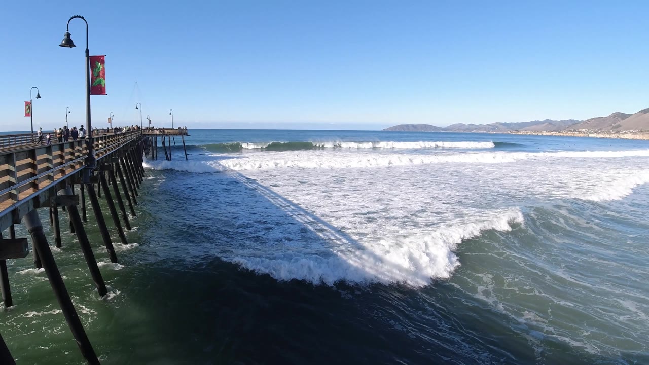 A larger sheet of surf fills the water beside the Pismo Beach pier, with the pier shadow stretching over the darker foreground water.