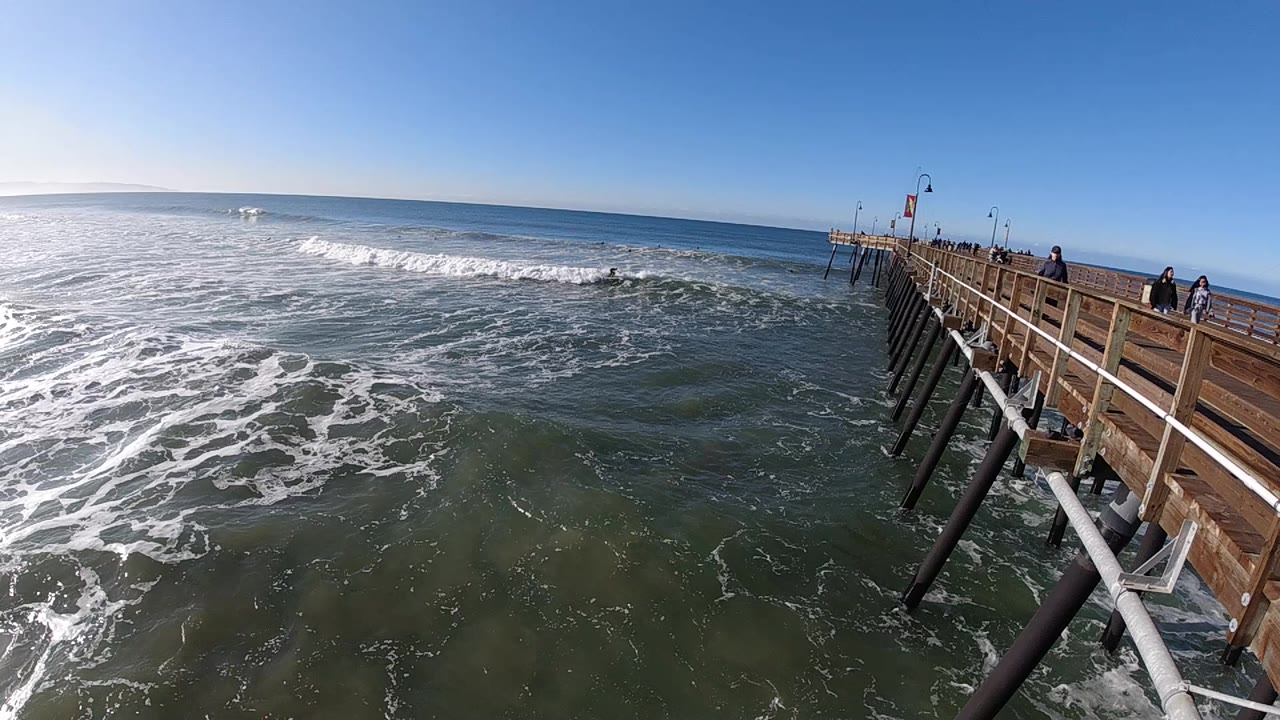 Surf rolls toward a wooden pier with blue sky above.
