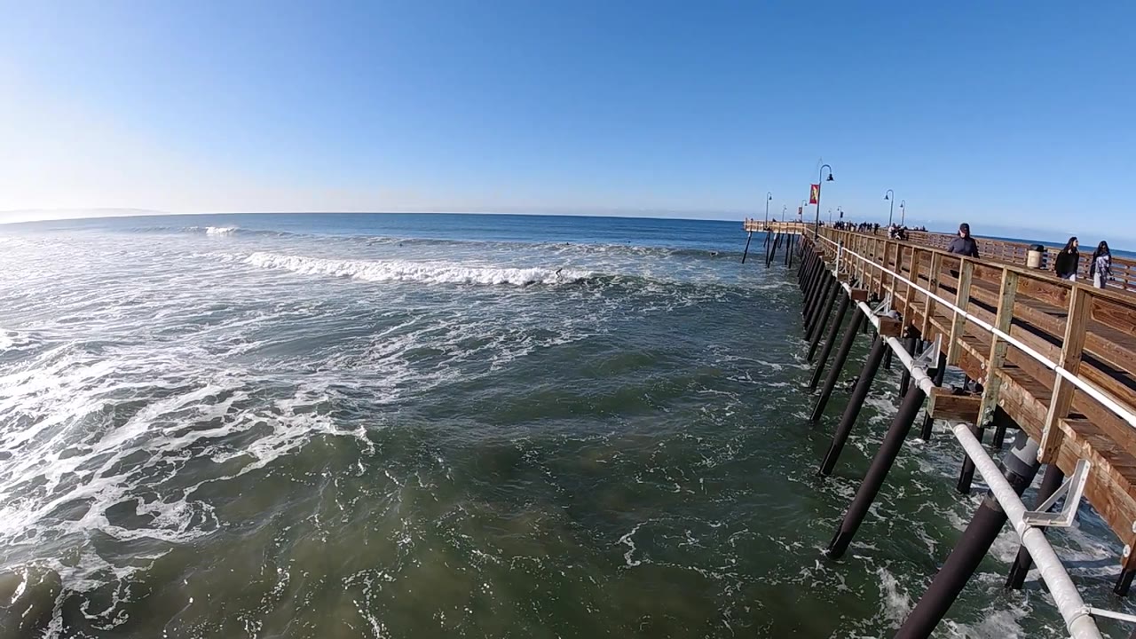 Wide ocean view with waves and a wooden pier at right.