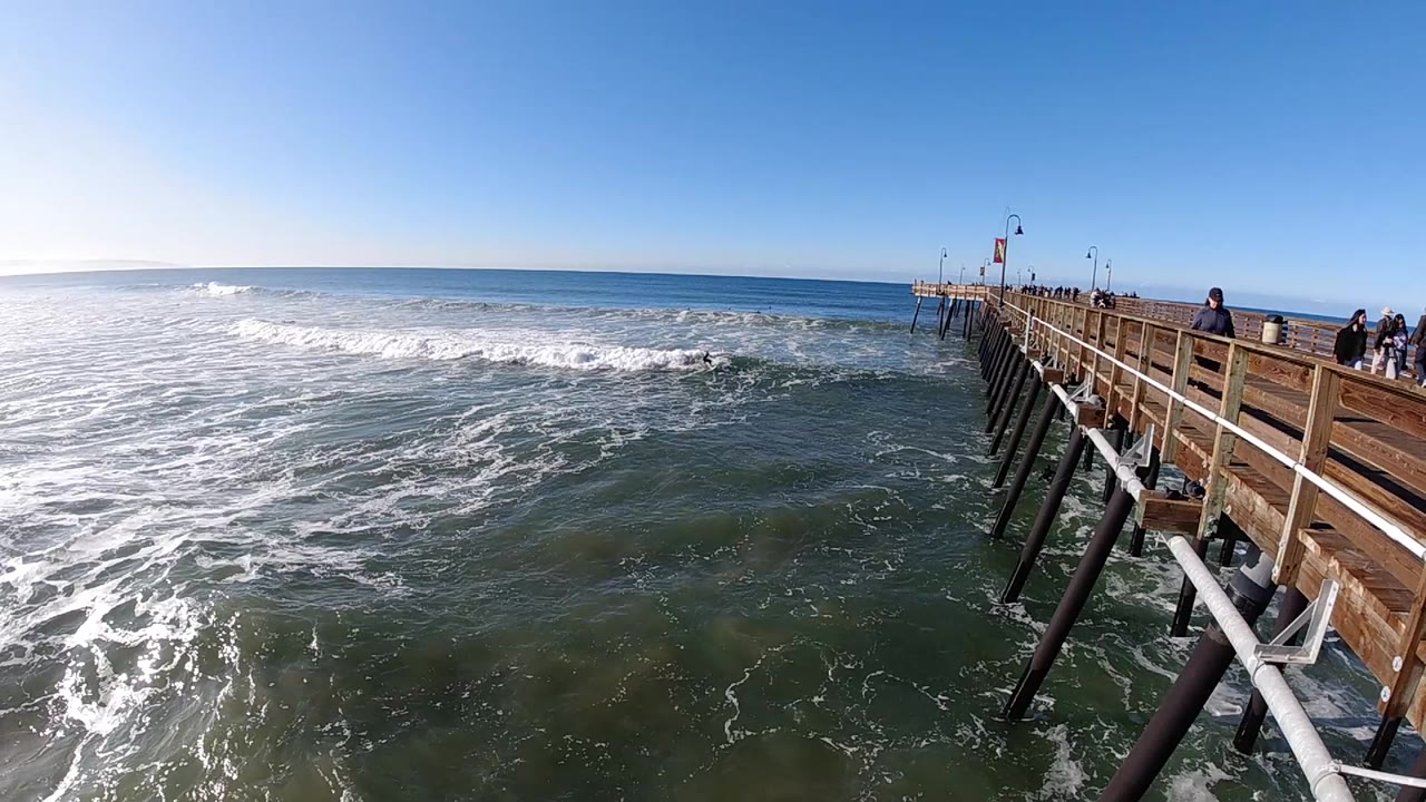 At 0:01, the Pismo Beach pier remains on the right as a broad line of whitewater breaks farther left and small figures gather near the railing.