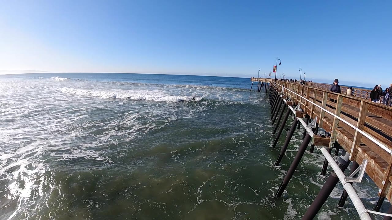 Wooden pier over choppy water with a wave breaking beyond it.
