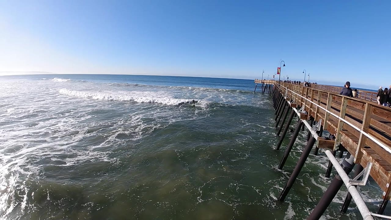 Pismo Beach pier fills more of the right edge as broken whitewater spreads across the left and center beneath a clean horizon.