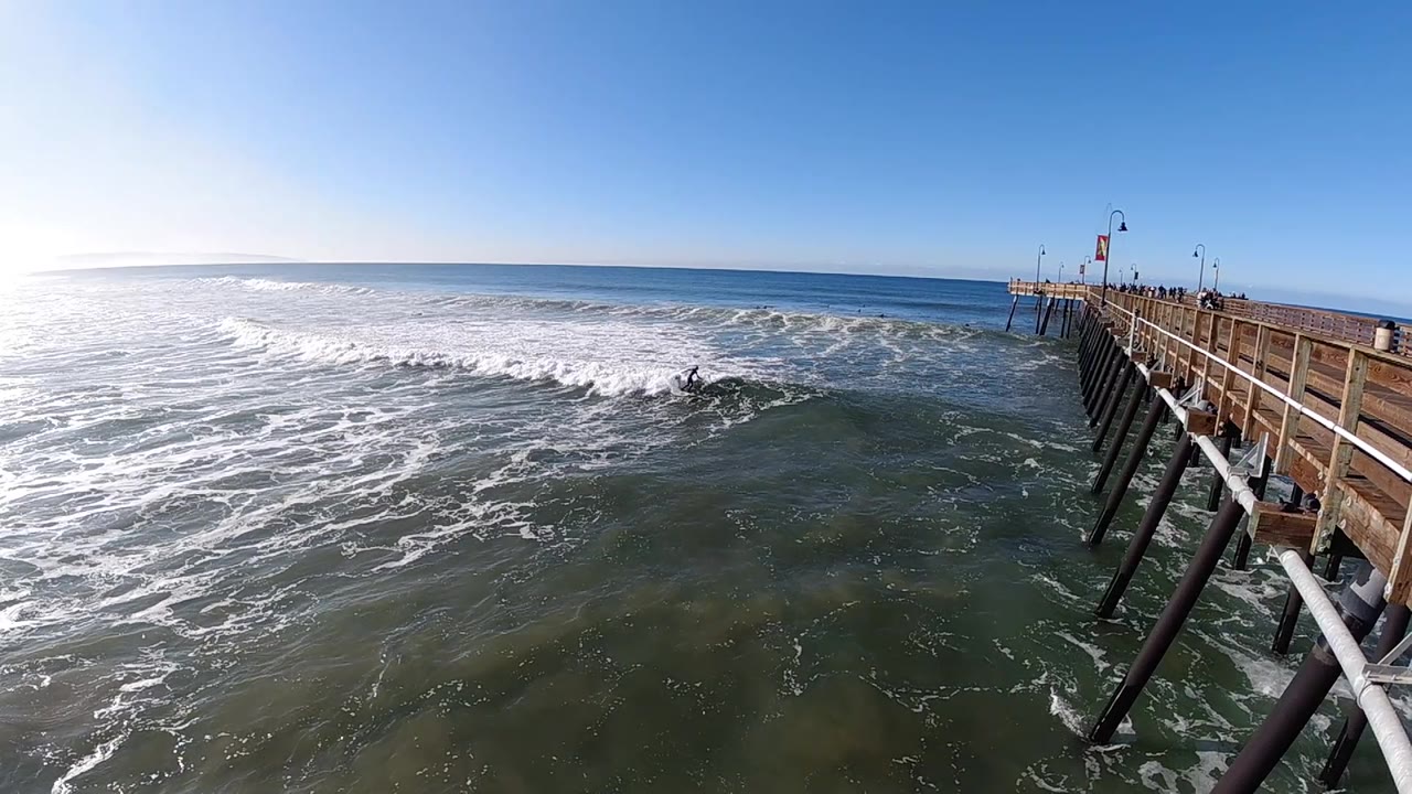 Wide coastal view with foamy water and pier on the right.