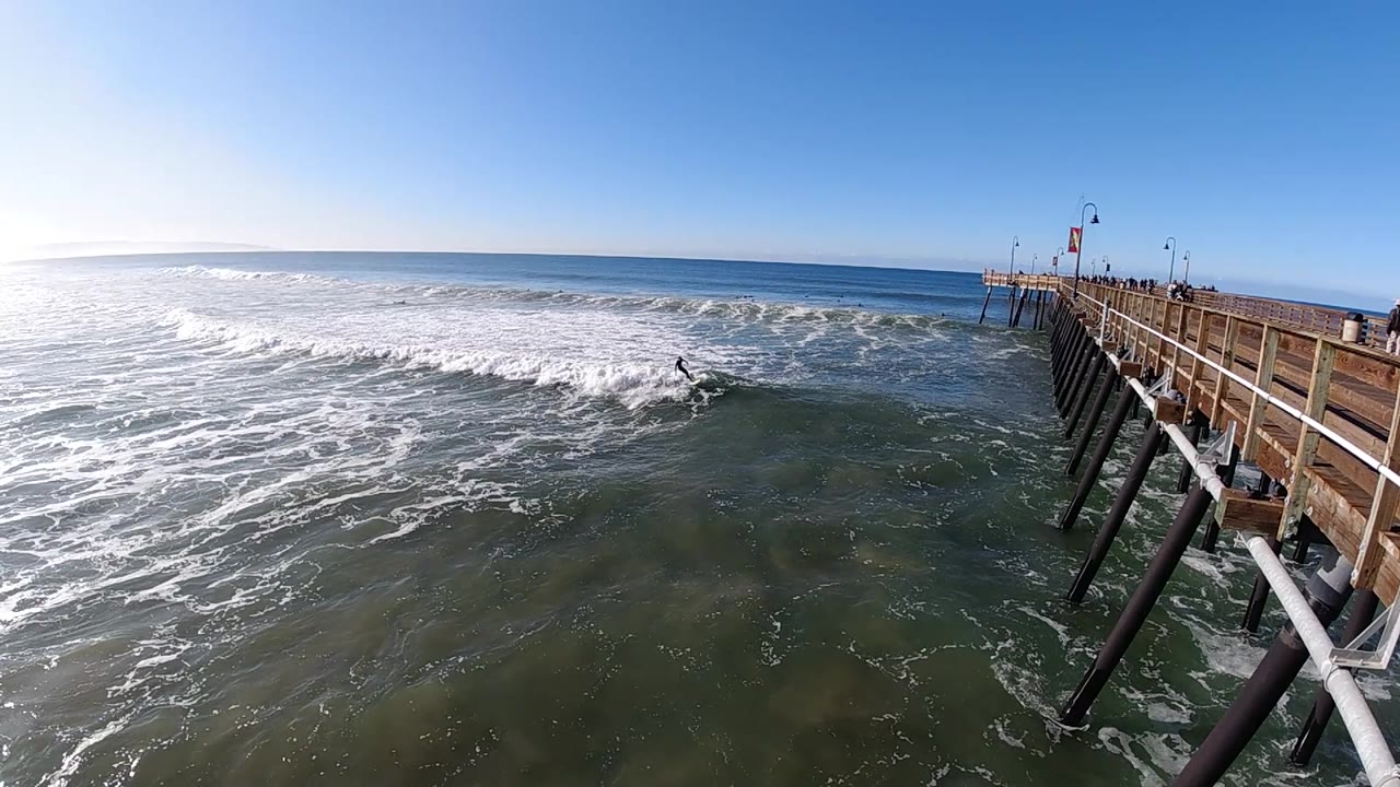 Wide ocean view with surfer and wooden pier.