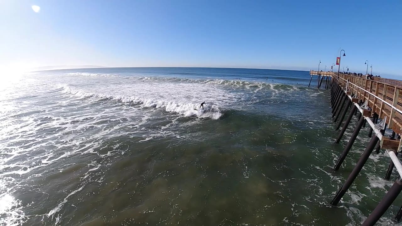 At 0:02 in Pismo Beach, California, the surf flattens slightly in the foreground while a low wave line crosses the midground and the pier recedes from the right.