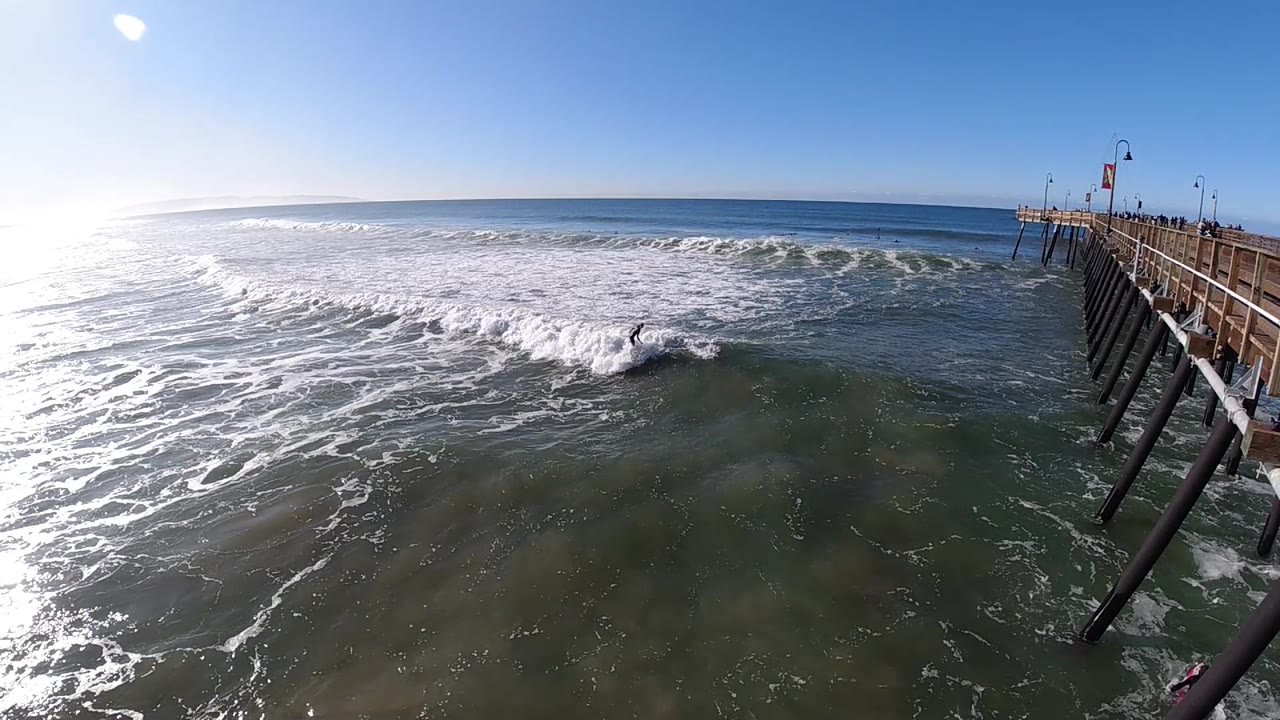 At two seconds, the wave has broken into a broad white sheet across the center while darker water remains in the foreground below the Pismo Beach pier.