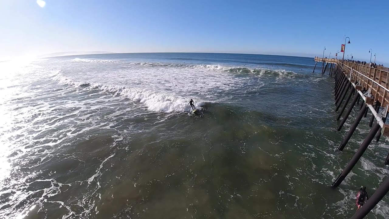 Surfer approaches a darker patch of water near the pier.