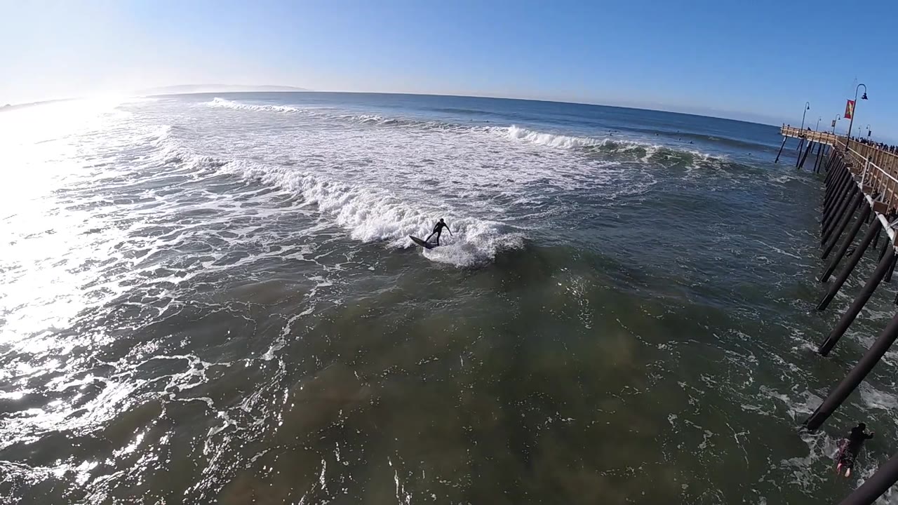 Surfer leans on a small wave beside the pier