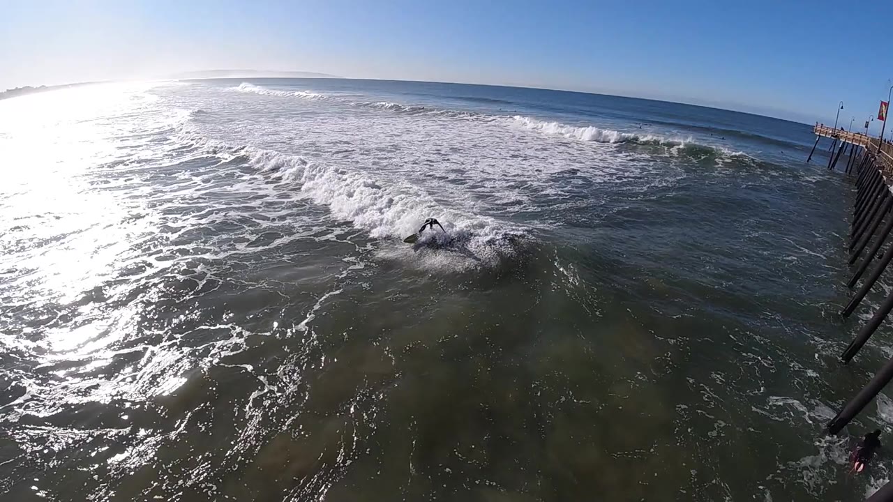 At 0:01, white foam advances through the center of the Pismo Beach water while the quay remains fixed along the right edge, with no visible people.