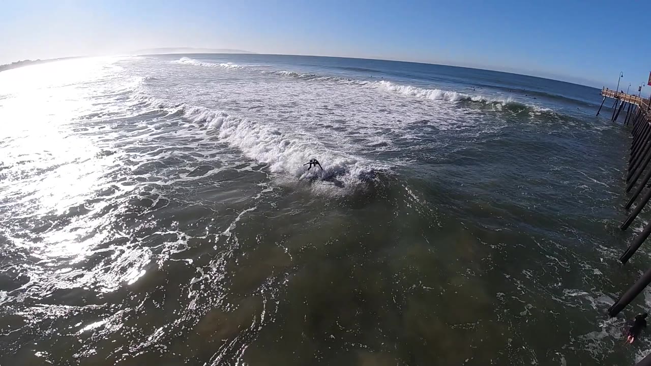 At 0:02, a breaking wave throws more foam across the foreground water at Pismo Beach as strong sunlight reflects from the left, with no visible people.