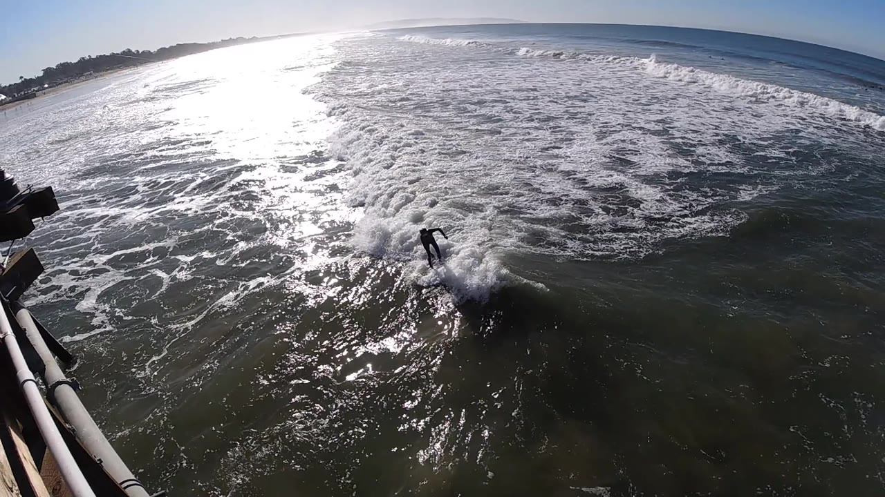 Water skier near a burst of spray with pier structure at the left edge.