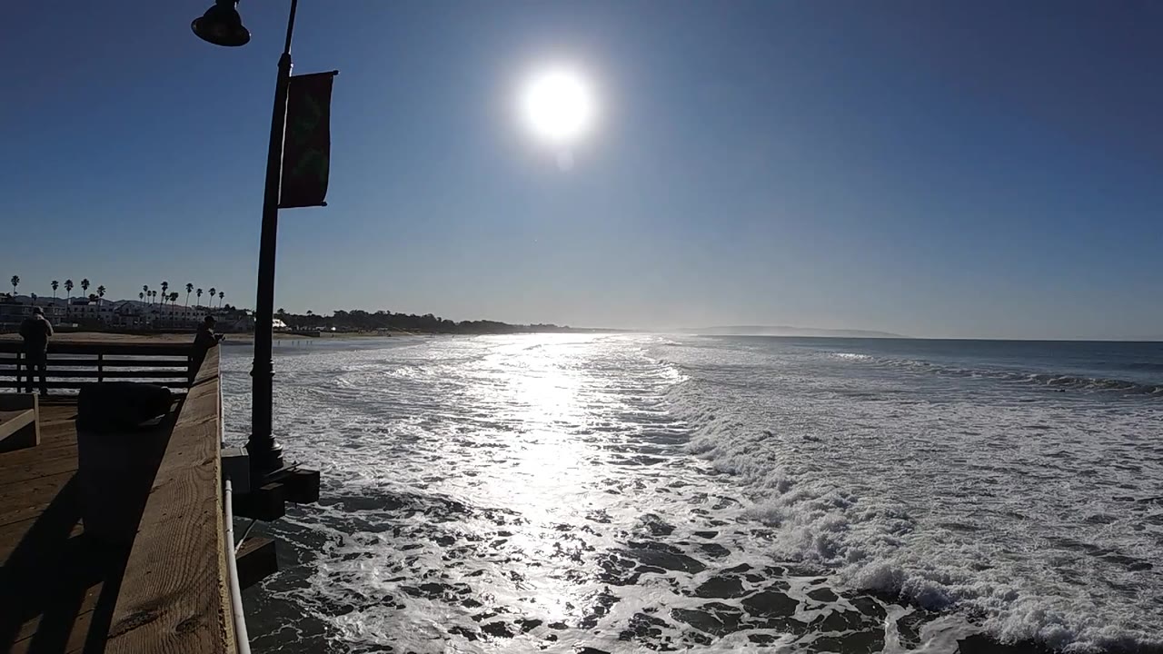 Open ocean stretches to the right while whitewater spreads across the foreground, the Pismo Beach shoreline sits low at left, and no visible people appear in the frame.