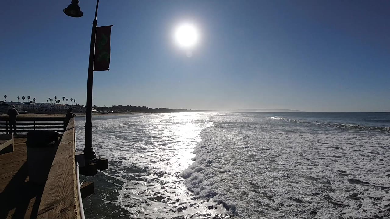 Pismo Beach waves spread farther across the sand while the bright sun reflects on the water near the center of the frame, with no visible people.