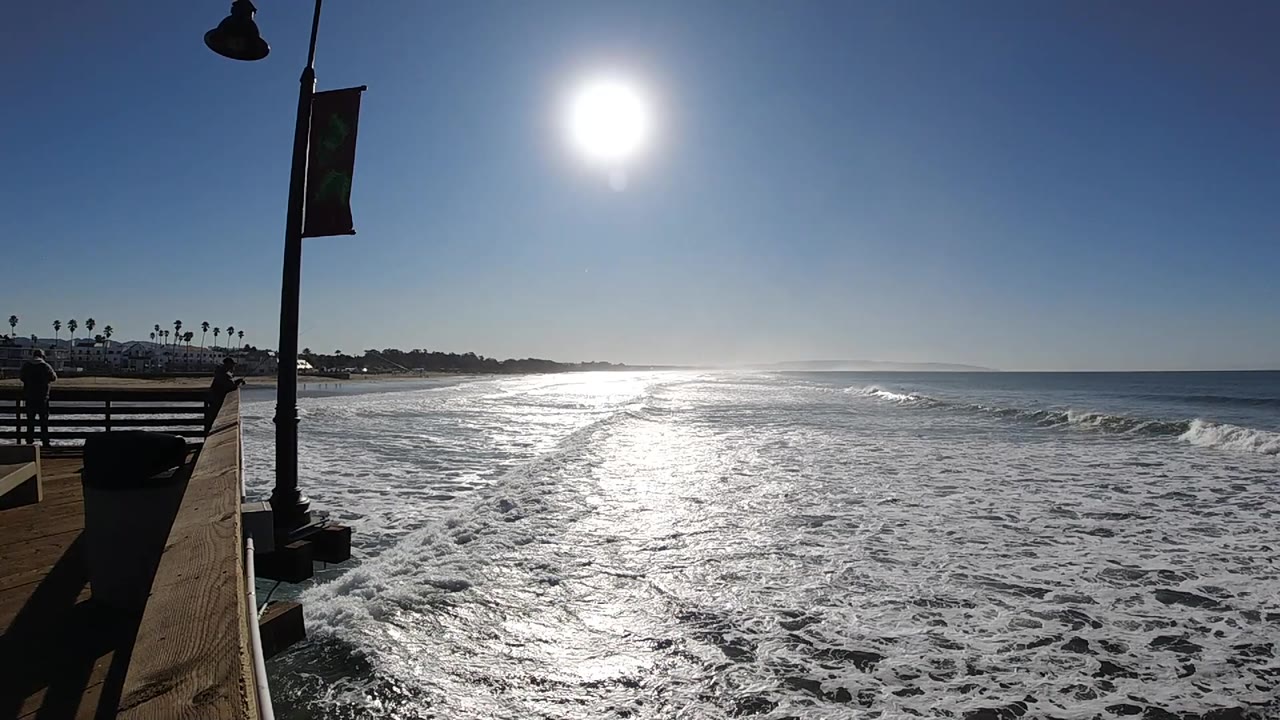 Ocean whitewater and sun glare viewed from a pier edge.