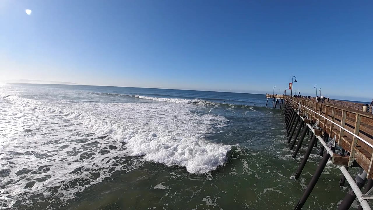At 0:02 in Pismo Beach, whitewater pushes farther across the lower frame as a darker band of ocean remains near the pier, with no identifiable people visible.