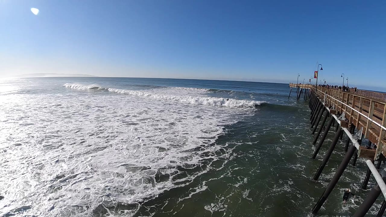 Pismo Beach waves break farther across the middle of the frame while the wooden pier stays tight to the right and no visible people appear.
